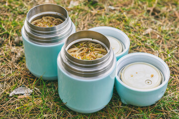 Warm food in a thermos standing on the grass - obrazy, fototapety, plakaty