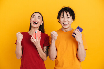 Young multiracial couple making winner gesture while using mobile phones