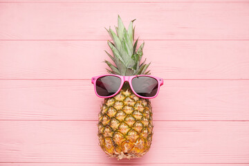Pineapple with sunglasses on color wooden background