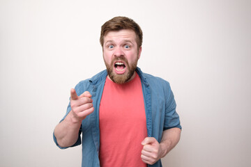 Aggressive bearded man yells and reproaches someone, he looks viciously, points his finger and blames. White background.