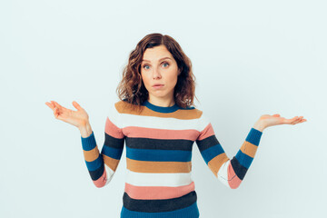 Young woman wearing casual striped sweater shrugs her shoulders