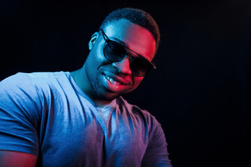 With sunglasses. Futuristic neon lighting. Young african american man in the studio