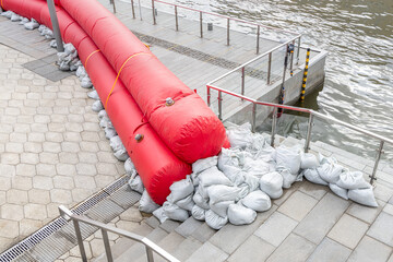 Water-filled cylindrical booms and sandbags protect city embankment against the water flood....