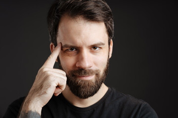 Bearded brunette man touching his temple and looking at camera
