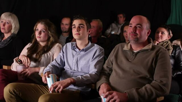 Caucasian family sat in Cinema Theatre watching a film or movie whilst eating popcorn. Tracking Shot. Stock Video Clip Footage