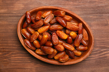 Plate with sweet dried dates on wooden background