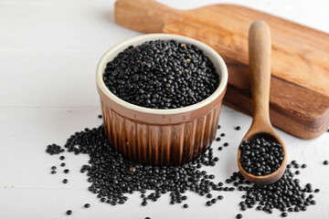 Bowl and spoon with black lentils on light background