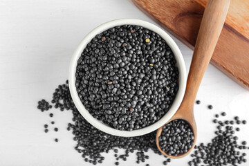 Bowl and spoon with black lentils on light background