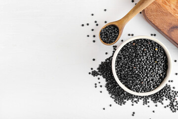 Bowl and spoon with black lentils on light background