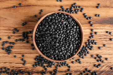 Bowl with black lentils on wooden background