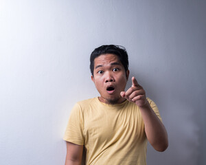 Portrait of Young Asian man with face expression, shocked, pointing finger, disappointment, weird and wow. Isolated background. Copy space, selective focus
