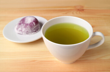 Closeup a Cup of Japanese Green Tea with Blurry Purple Sweet Potato Daifuku or Red Bean Paste Filling Rice Cake in Backdrop