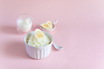 Rice porridge on vegetable milk with banana slices on a pink minimal background. Diet healthy Breakfast