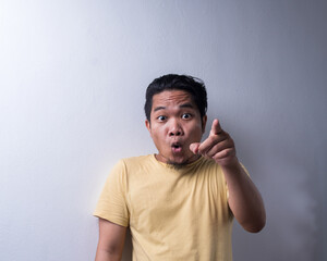 Portrait of Young Asian man with face expression, shocked, pointing finger, disappointment, weird and wow. Isolated background. Copy space, selective focus