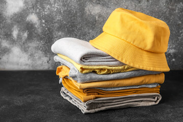 Stack of stylish clothes with hat on grunge background