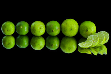 Many limes in a line with lemon slices in front of the lime and the limes reflection on a black background, a beautiful wallpaper of fresh and juicy limes