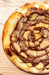 Banana pizza with chocolate sauce and cinnamon powder, served on a wooden table. View from the top.