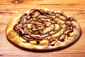 Banana pizza with chocolate sauce and cinnamon powder, served on a wooden table. View from the top.
