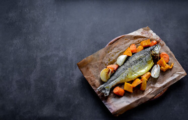 Trout baked whole in spices with vegetables-pumpkin and onion. In baking paper on a wooden board. Black background, copy space