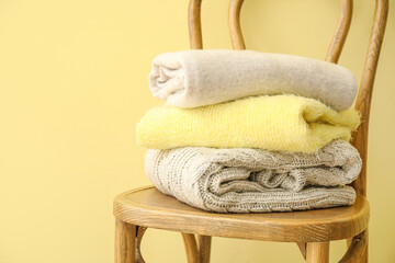 Chair with stack of stylish clothes on color background