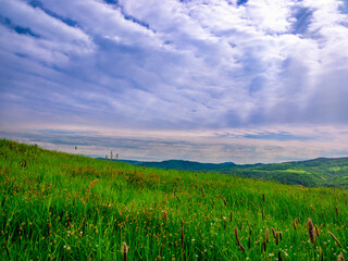 Spring meadow and hills in the distance with cloudy skies and sun rays penetrating through the clouds