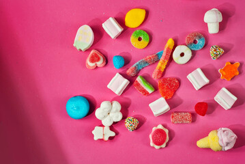Lots of colorful candies on a pink background. Sweets close up. The concept of childhood and holidays. Copy space and free space for text near sweets.