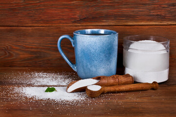 Blue ceramic cup, glass jar with wooden scoops of sorbitol and fructose on a wooden background. Different sweeteners concept.