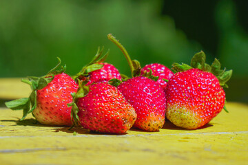 Red strawberries on an old yellow wooden table in garden