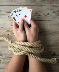 Hands of man are tied with a rope and in his hands he holds playing cards, concept addiction, Gambling addiction