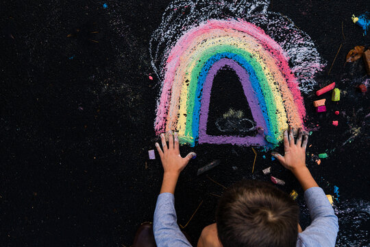 Overhead view of boy drawing rainbow art with chalk on pavement