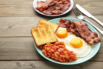 Traditional full English breakfast - fried eggs, beans, bacon and toast on grey wooden background with copy space for text.