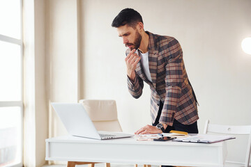 Works in the office. Young stylish businessman in suit indoors. Conception of success