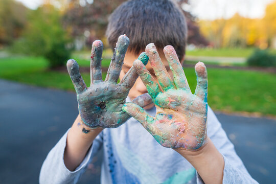 Young boy holding up hands covered in paint