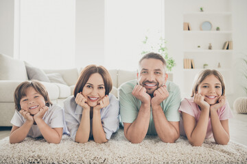 Photo of optimistic nice family mom dad two kids hands face lie on floor wear t-shirts at home