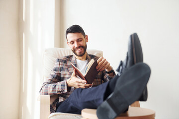 Naklejka premium Reads book. Young stylish businessman in suit indoors. Conception of success