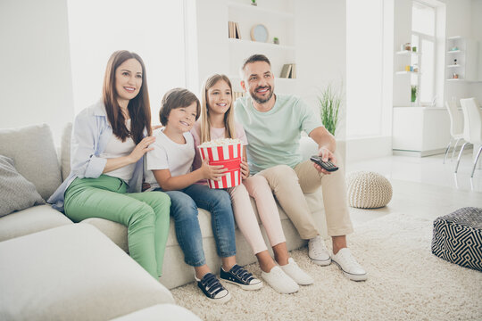 Full Size Photo Of Optimistic Cute Family Brunette Mom Dad Two Kids Watch Tv Sit On Sofa Wear T-shirts Trousers At Home