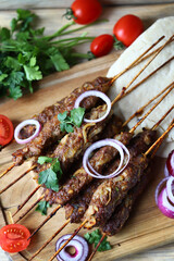 Appetizing lula kebab on wooden sticks with onion rings and herbs. Lula kebab preparation. Ramadan.