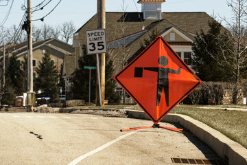 Bright orange and black flagger or flagman sign on the side of the road