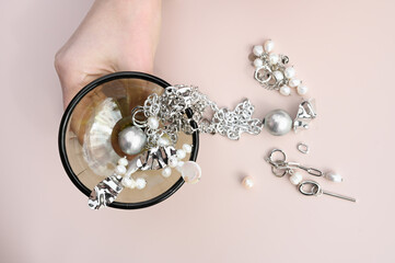 Glass goblet with stylish jewelry set of different earrings and chains in women's hand. Creative idea of jewelry display