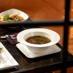 Meat soup with dill on dining table with cutlery on it. View through restaurant window. Nutritious wholesome food. Delicious and healthy lunch or dinner.