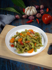 Tumis or oseng Pare or Stir-Fried Bitter Gourd, typical Indonesian home dish. Served in white plate with ingredients as background. 