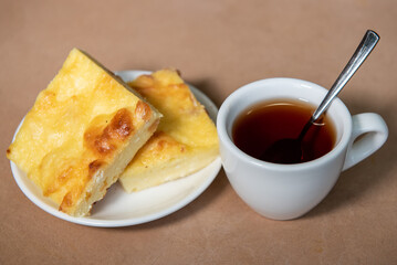Tea in a white cup with a curd casserole on a saucer. Breakfast. Close-up. Selective focus.