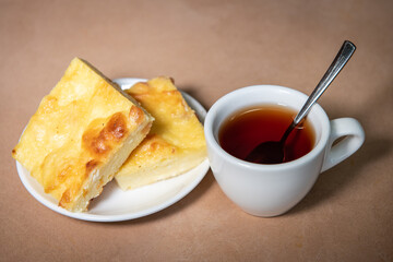 Tea in a white cup with a curd casserole on a saucer. Breakfast. Close-up. Selective focus.