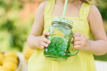 Child Girl drink natural lemonade at stand in park. Summer refreshing natural drink lemonade. Detox fruit infused flavored water, cocktail in a beverage dispenser with fresh fruits