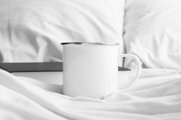 Enamel mug mockup with a book on the bed.