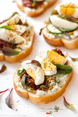 Several sandwiches with egg, creamy sauce and sun-dried tomatoes on a white wooden background top view. Tasty rustic breakfast.