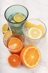 Lemonade with lime, lemon and orange on white marble table with orange and green glass