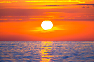 Fototapeta na wymiar Sun rising in the sea with a fishing boat in the rays of the sun above the waves. Beautiful sunrise on the ocean with a big and colorful sun in summer. A new day begins.