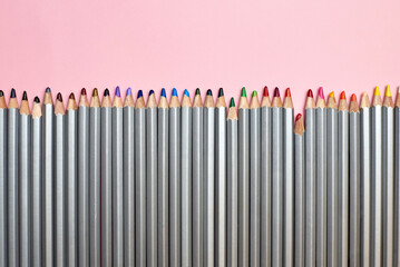 Colored pencils lined up in a row on a pink background.