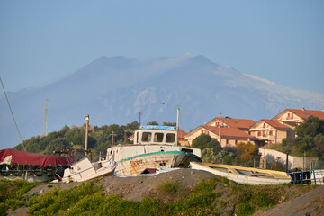 Etna volcano seen from the port with an old fishing boat in the foreground
